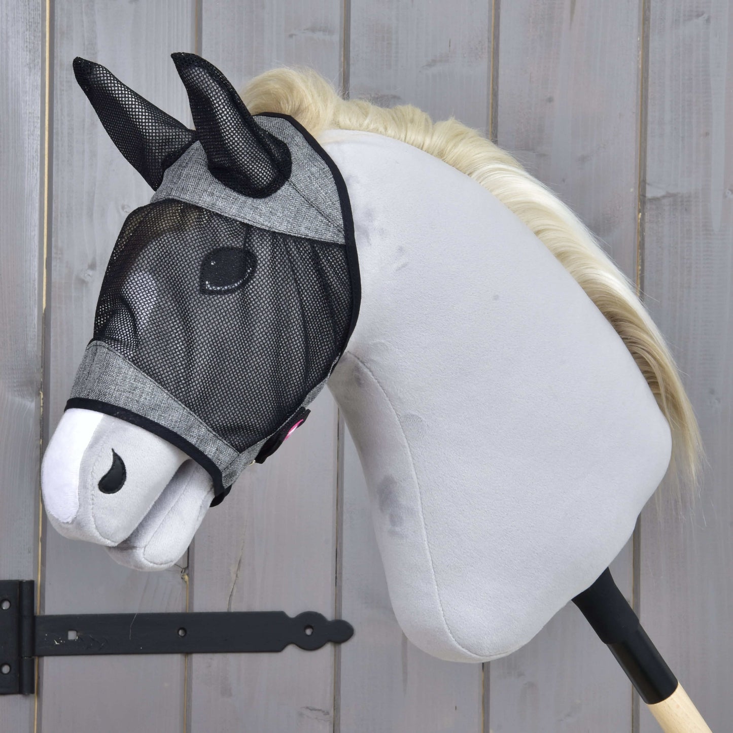 Masque anti-mouches De Luxe Gris Clair de Hobby Horse LarDen protégeant un hobby horse en peluche au corps gris clair, museau blanc et nez noir, présenté devant des panneaux en bois. Le masque a un tissu lavable et une bordure grise.