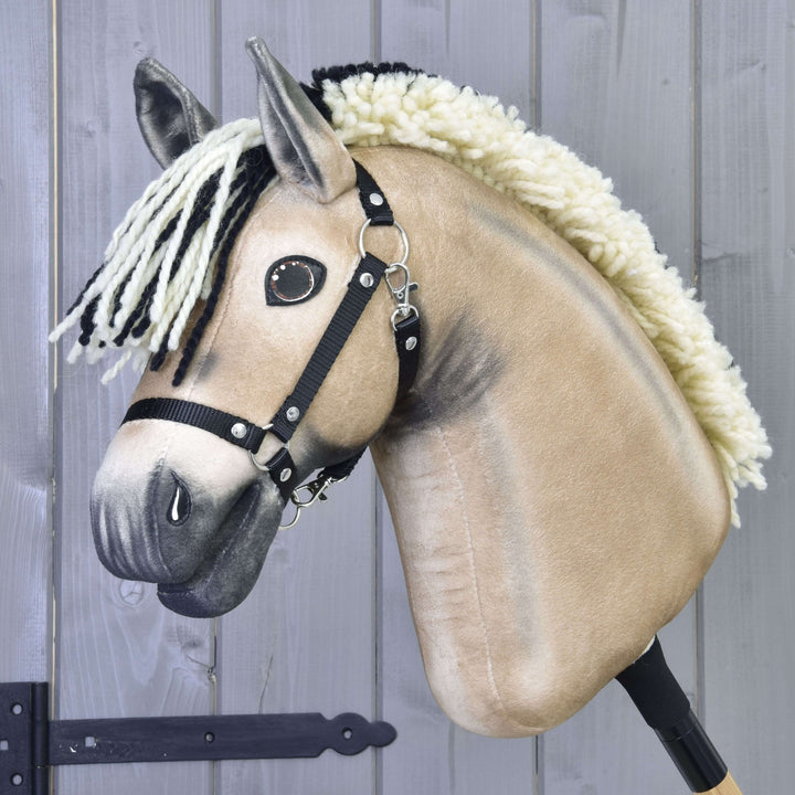 Gros plan sur le Hobby Horse Ozzy avec licol noir beige de Hobby Horse LarDen, avec crinière en fil noir et blanc, licol noir et yeux en bouton, monté sur un bâton devant un fond en bois gris.