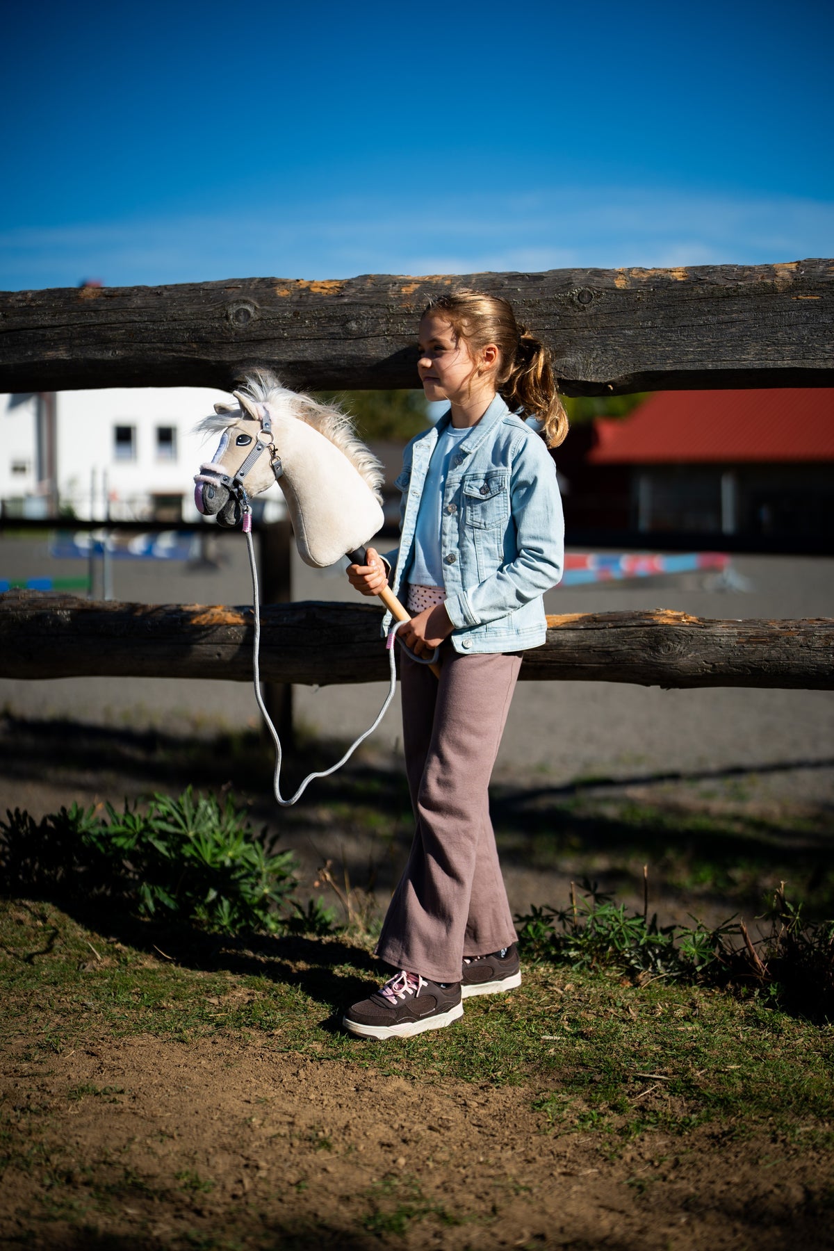 Jeune fille en veste en jean près d'une clôture en rondins tenant le Hobby Horse Pixie avec un licol gris à fourrure et une longe