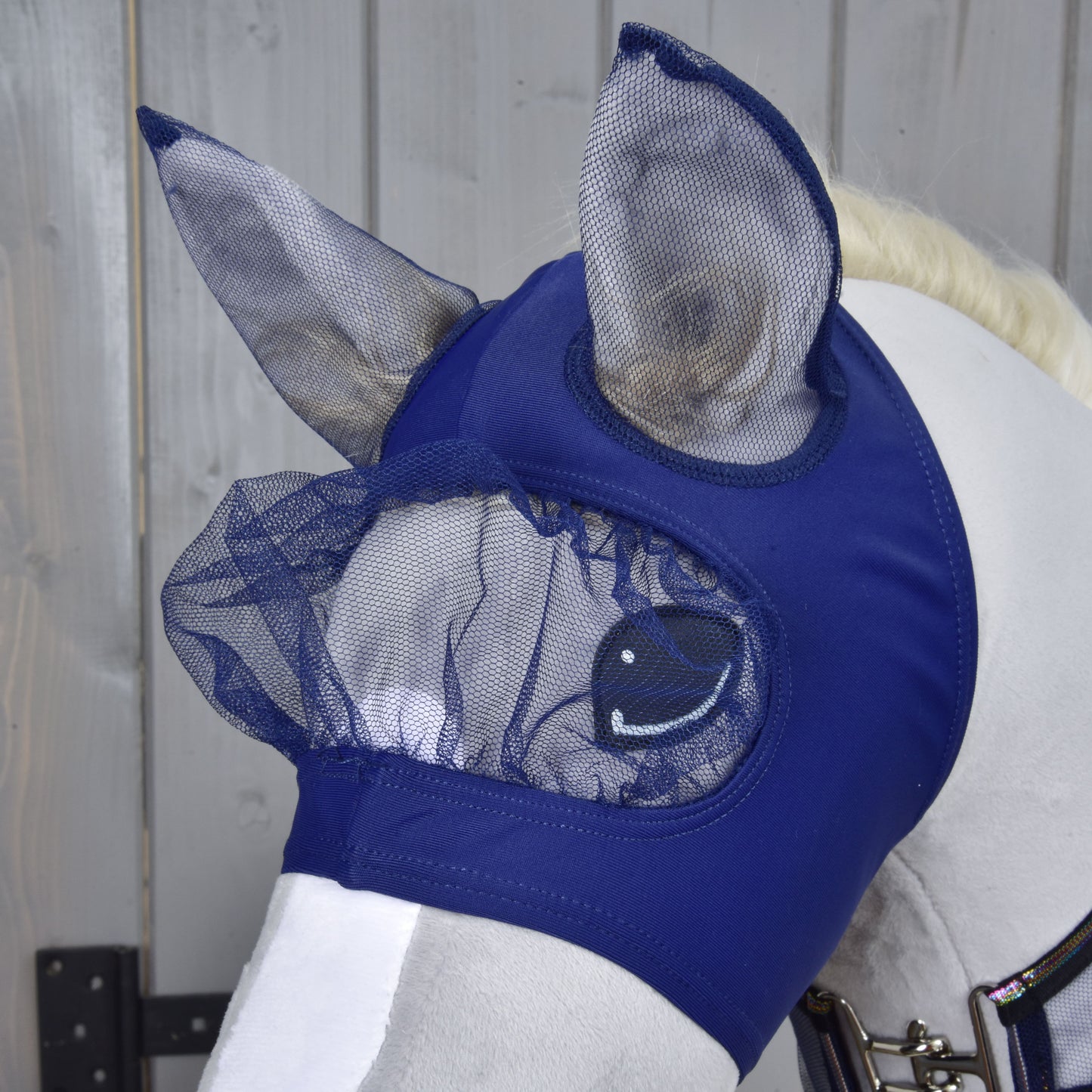 A white horse wears the Hobby Horse LarDen Set Fly Combo in navy blue, featuring mesh ear and eye covers. Perfect for hobby horsing style, this mask protects your horse's eyes and ears from insects.