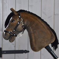 Hobby Horse Sundance avec licol noir de Hobby Horse LarDen, avec design en peluche, crinière en fil noir, bride et rênes, capturant l’allure fougueuse d’un étalon Pur-sang anglais, monté sur un bâton devant un mur en planches de bois clair.