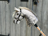 Hobby Horse Untamed Sweety avec licol noir de Hobby Horse LarDen, Hobby Horse gris en peluche sur un bâton en bois, présenté devant une porte en bois patinée avec charnières métalliques et cadenas.